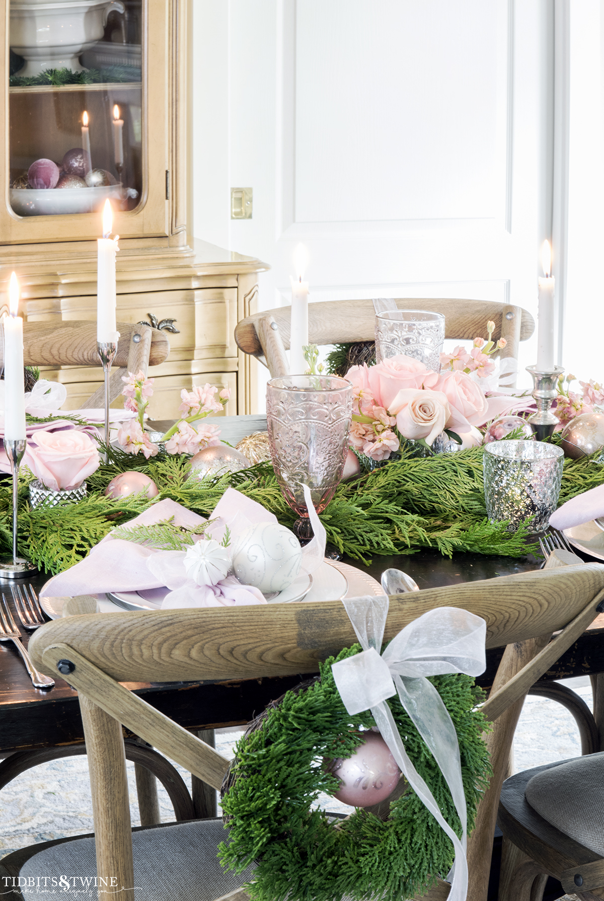 pink and silver Christmas tablescape with greenery and roses and chairs with small wreaths on the backs