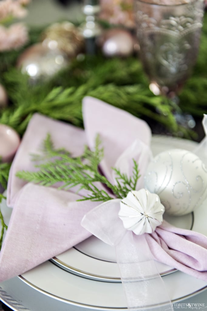 Closeup of christmas place setting tied with ribbon two white ornaments and cedar garland