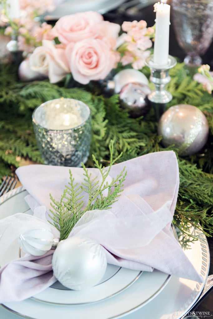 Christmas place setting with pink napkin tied with white ornaments and cedar sprig