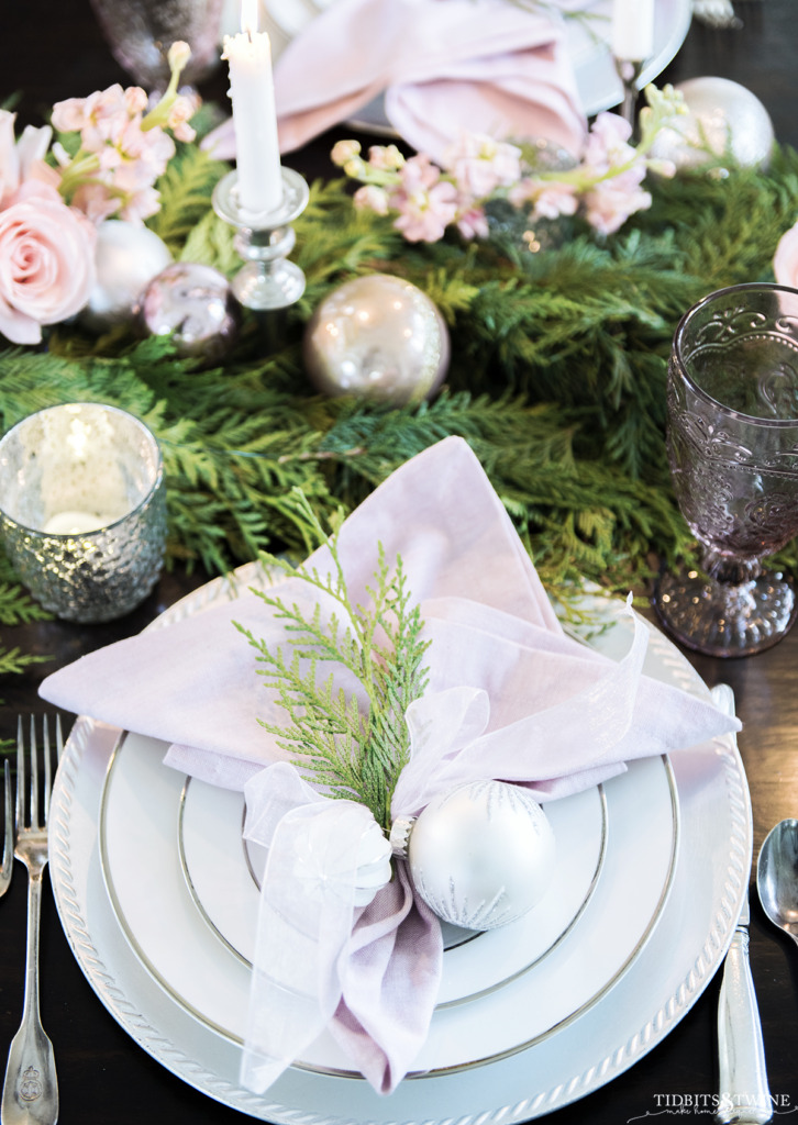 Christmas place setting with pink napkin tied with white ornaments and cedar sprig