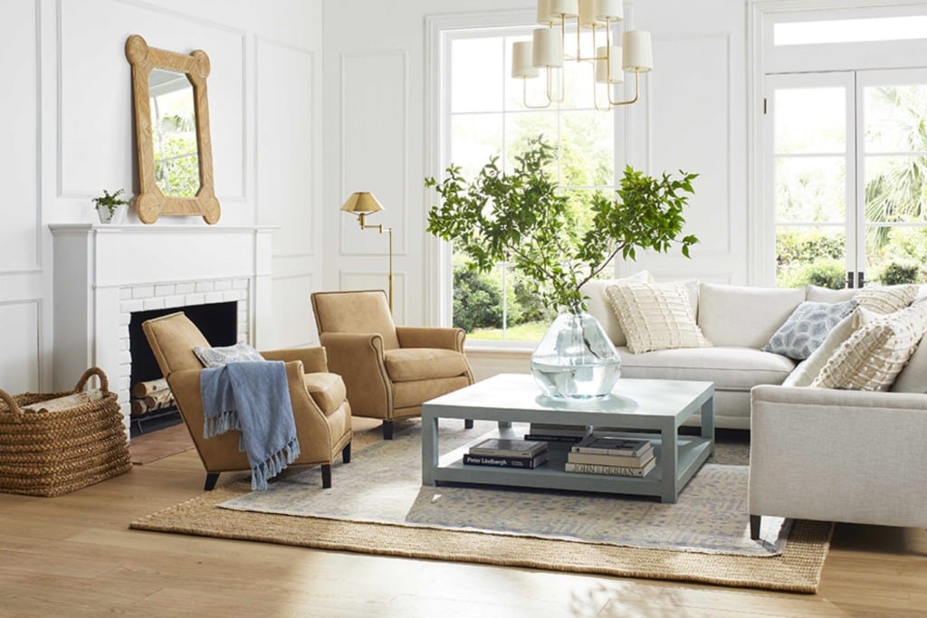 White living room with picture frame molding and white sectional with tan side chairs and oversized coffee table