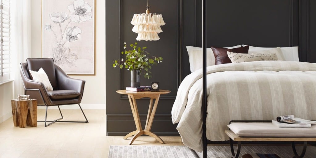 Dark brown bedroom wall with four poster bed and nightstand with light wood floors