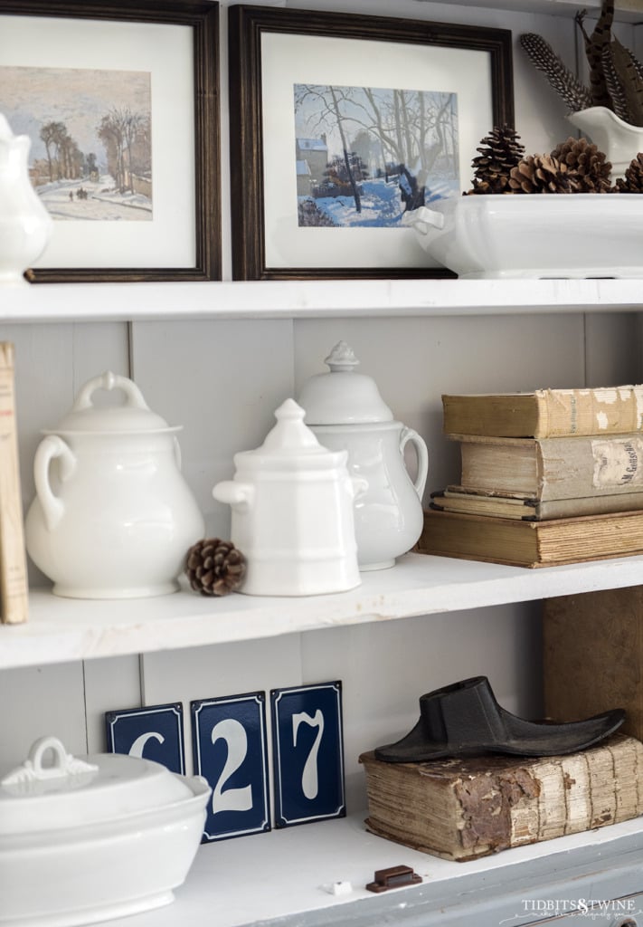 Closeup of white ironstone and winter artwork on white bookshelves