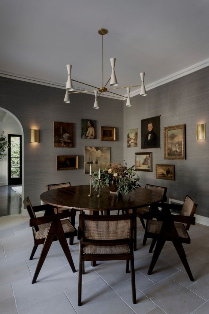 Gray grasscloth dining room with dark wood round table and modern light fixture and antique oil paintings on wall