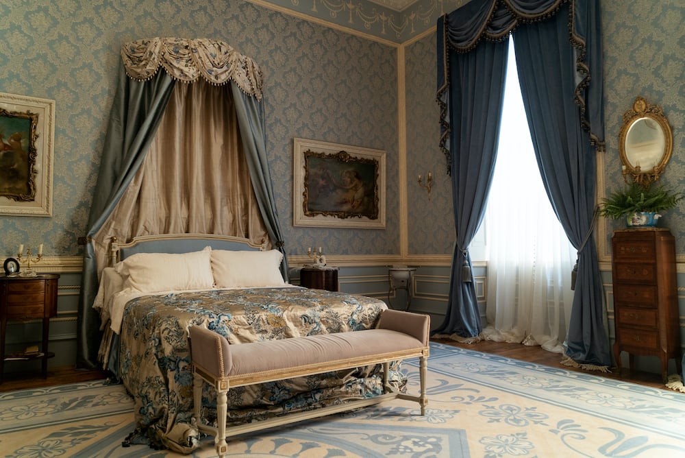 Netflix Bridgerton Regency style bedroom with blue wallpaper and bed with crown above