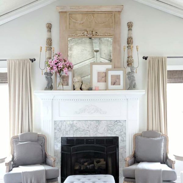 French living room with fireplace flanked by chairs and large candle sconces on either side of trumeau mirror