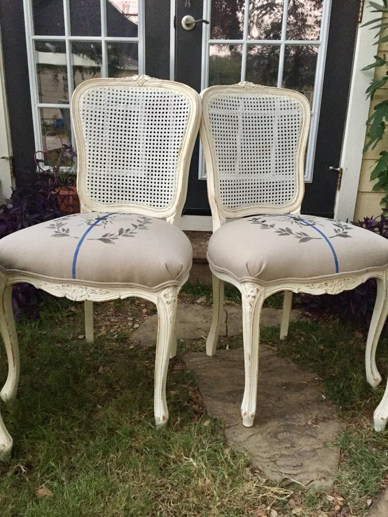 Two cream wood French antique dining chairs upholstered with grain sacks with laurel wreath and blue stripe