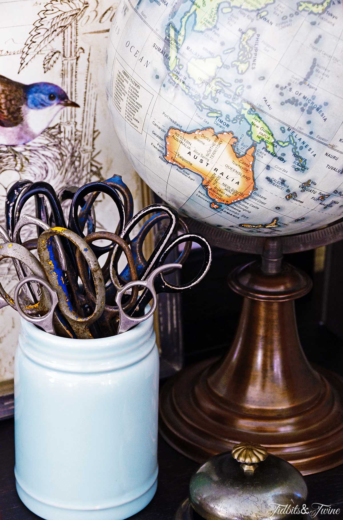 Closeup of antique scissors in a blue mason jar next to a globe