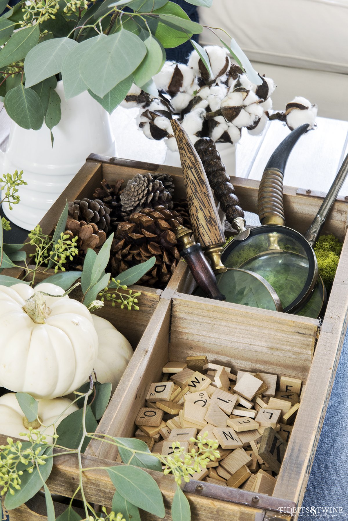 Wooden crate holding white pumpkins scrabble tiles and magnifying glasses