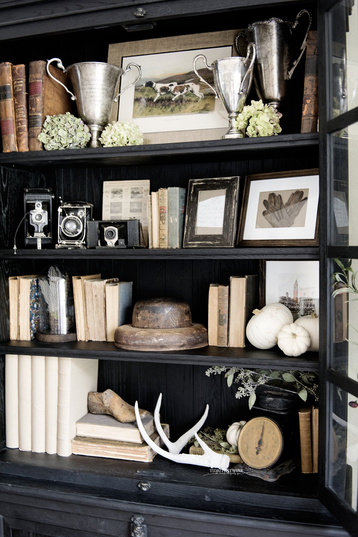 black french cabinet decorated for fall with antique books trophies and dried hydrangea