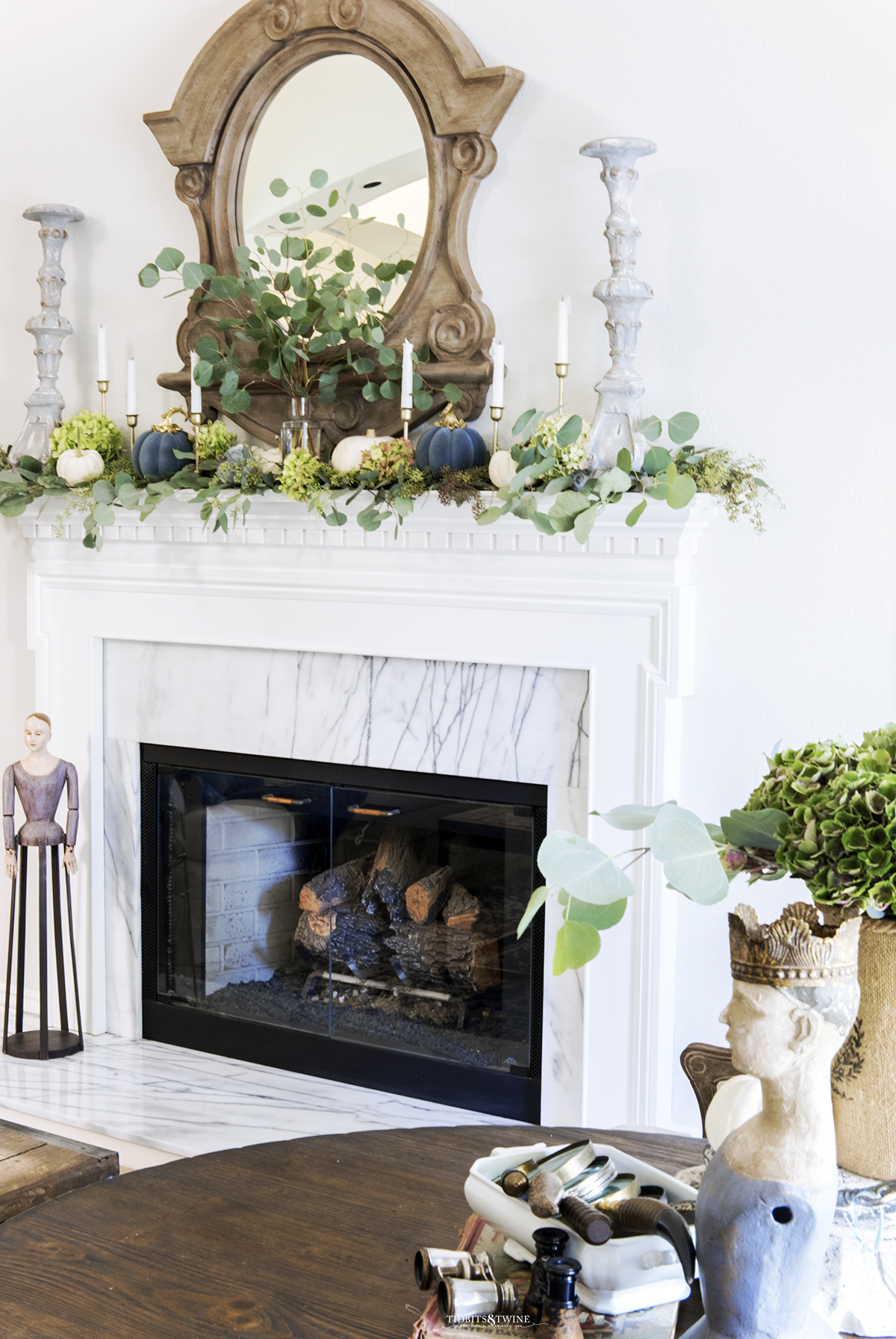 White fireplace mantel with French mirror above and eucalyptus and white pumpkins on top