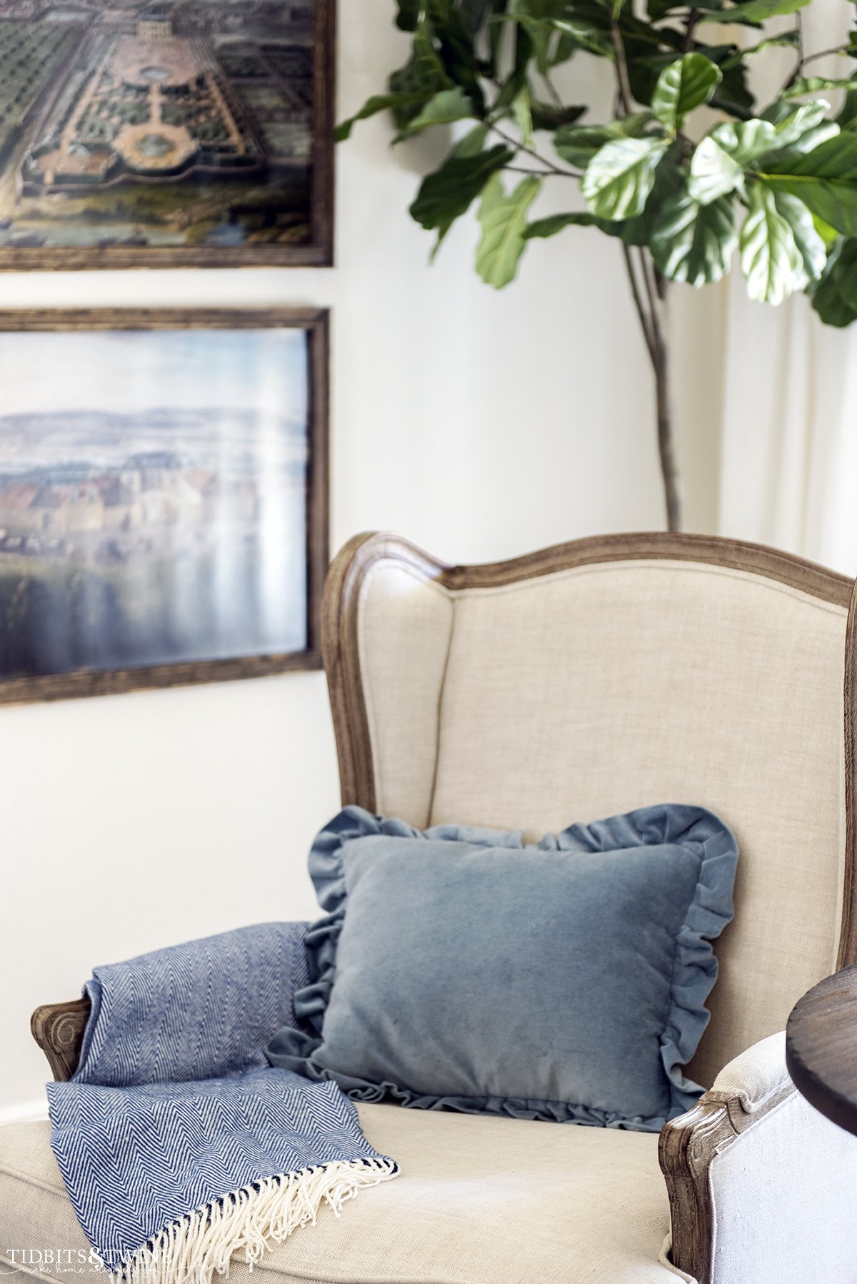 French wingback chair with blue ruffle pillow and artwork on walls