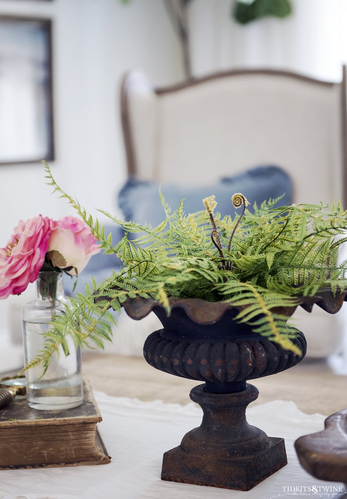 Iron urn with fake fern on coffee table with white runner and old book with pink rose