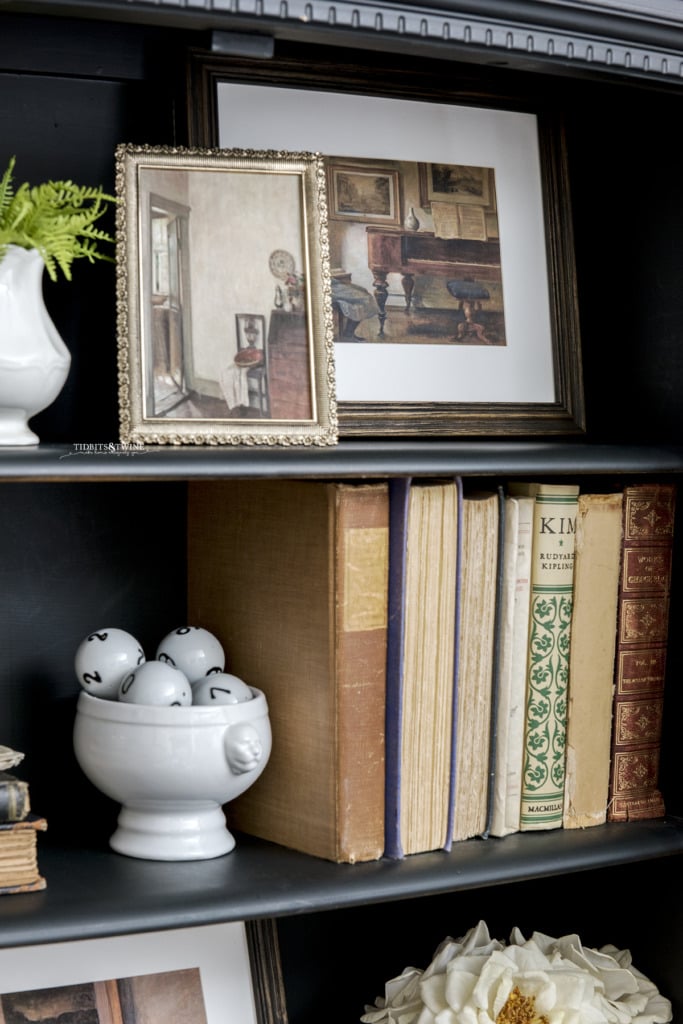 Closeup of black cabinet containing framed downloadable Carl Holsoe artwork and antique books