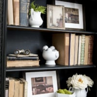 Black cabinet with shelves decorated with antique books framed artwork ironstone moss and fake white roses