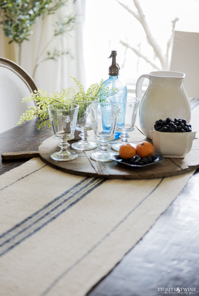 Blue stripe vintage grain sack table runner with antique bread board holding glasses fruit and a pitcher