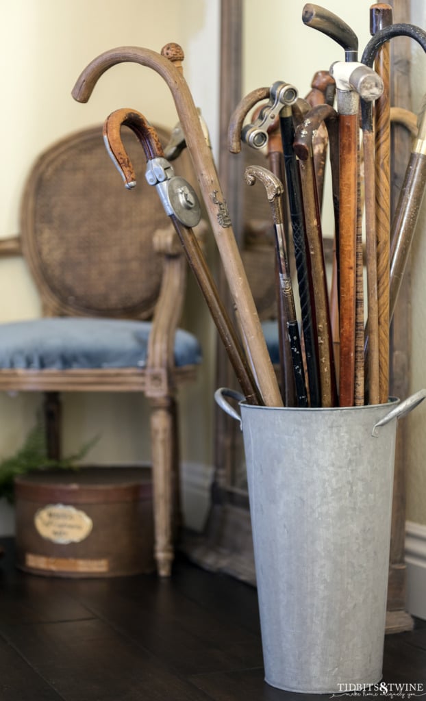 Antique cane collection in metal bucket in entryway with chair in background