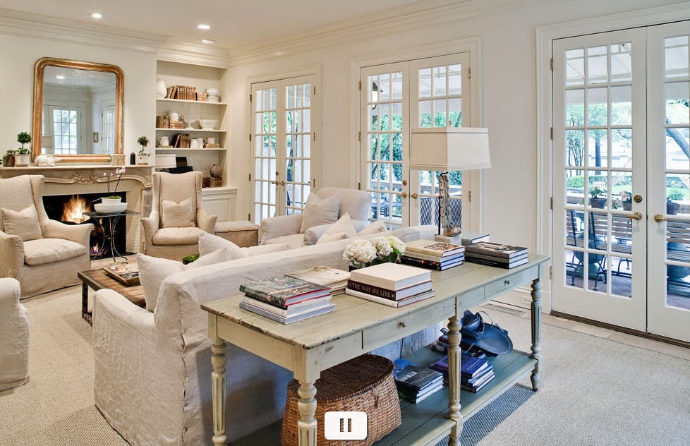 white french living room with large sofa table stacked with books and built ins by fireplace