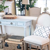 blue french sofa table with french linen chair on the side with baskets and books underneath and french wingback chair in background