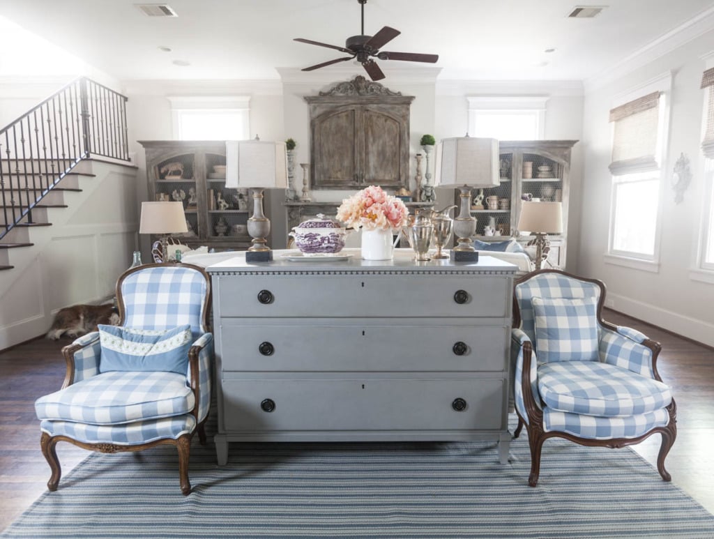 gray chest of drawers with blue and white check chairs on either side behind a sofa in a french living room