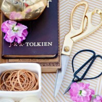 tray holding gold scissors and antique scissors with a gold vase holding pencils some purple flowers and white container of rubber bands