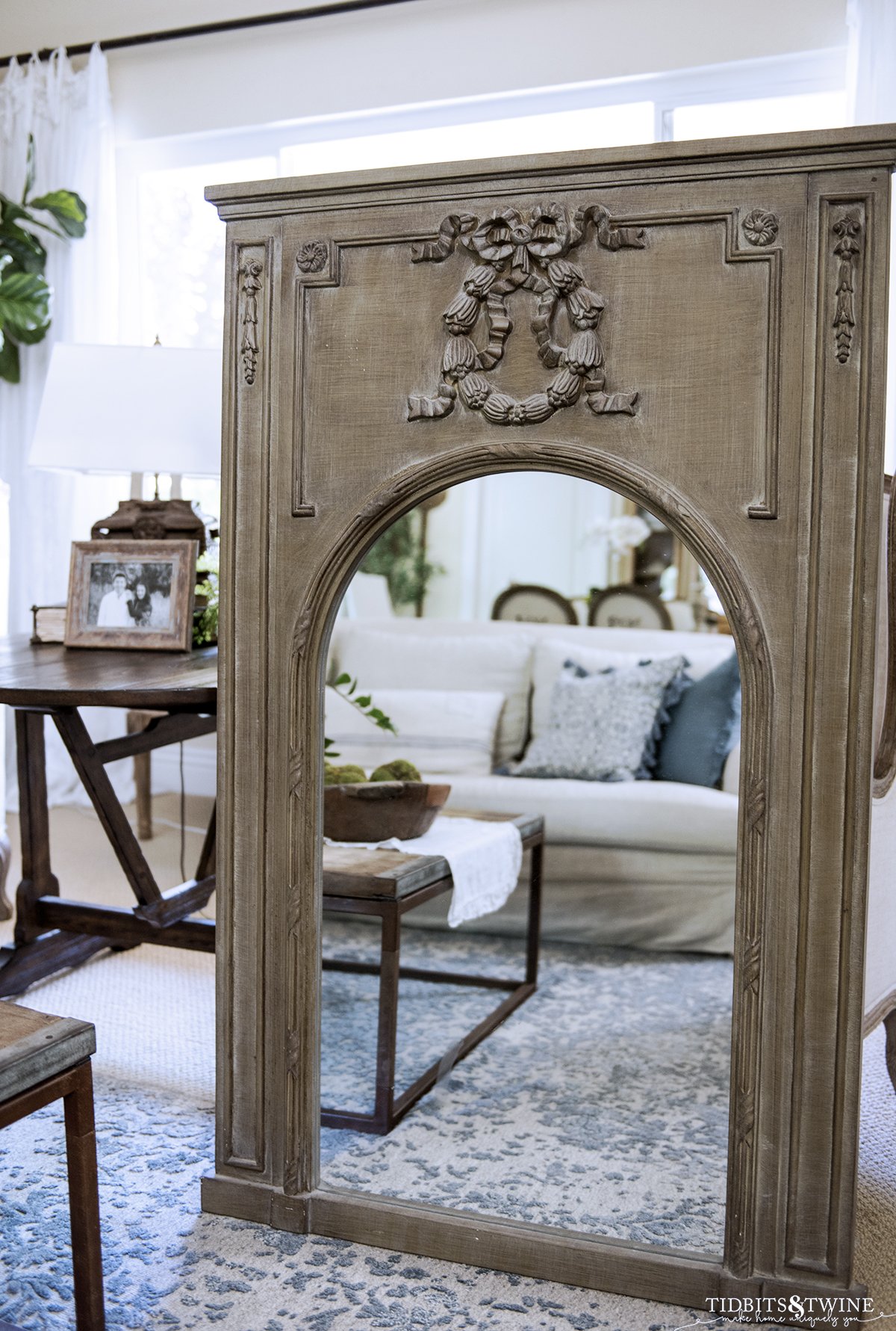 green distressed trumeau mirror with arched mirror propped up in a living room