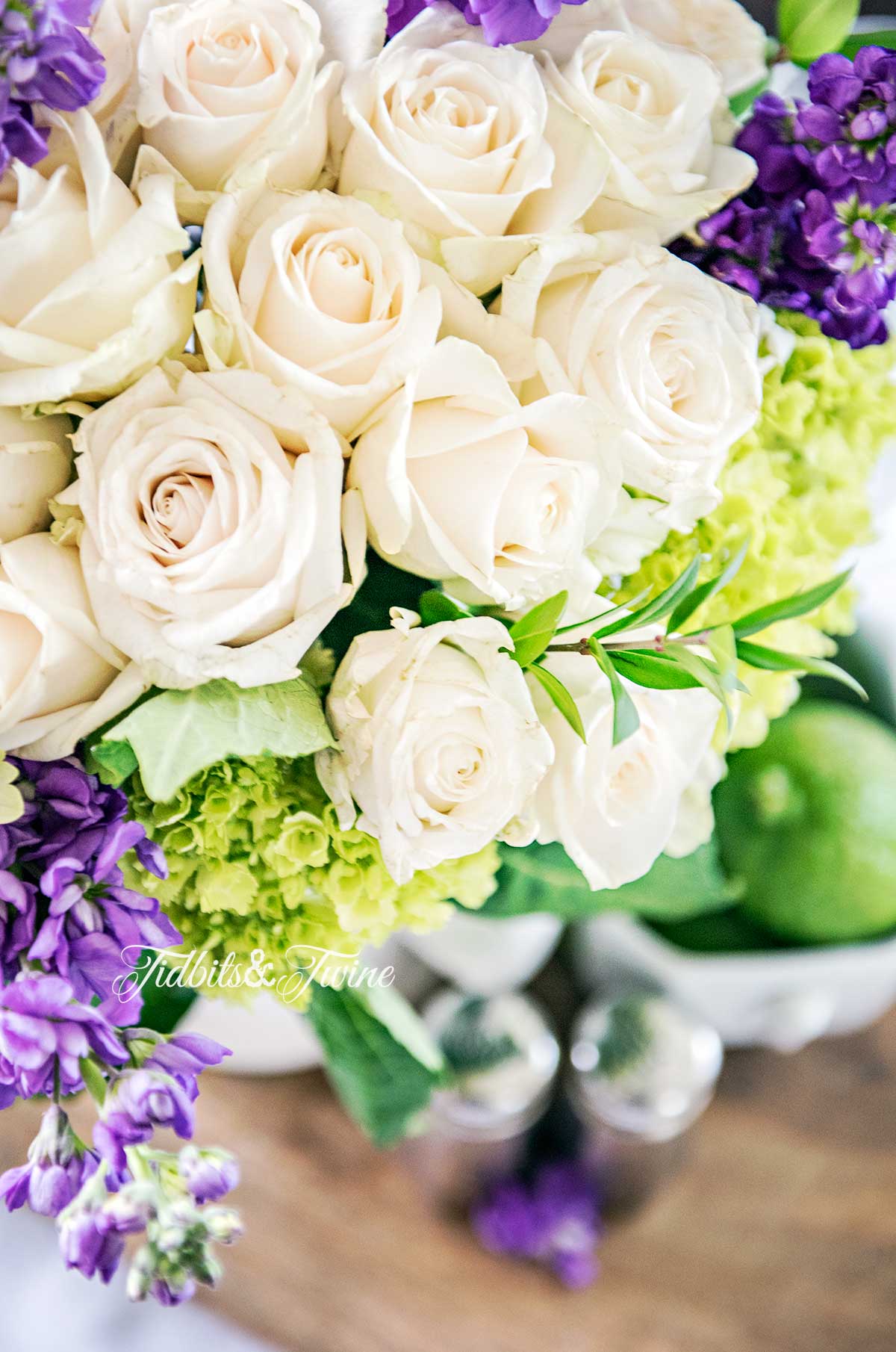 looking from above white roses with purple stock and green hydrangea with limes in an ironstone bowl beneath