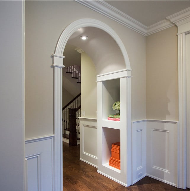 hallway painted natural cream with white wainscotting and arched doorway trimmed with molding and wood floors