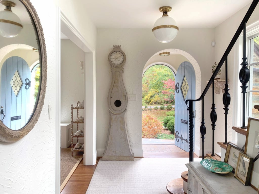 white walled foyer with gray mora clock next to arched front door that is painted blue