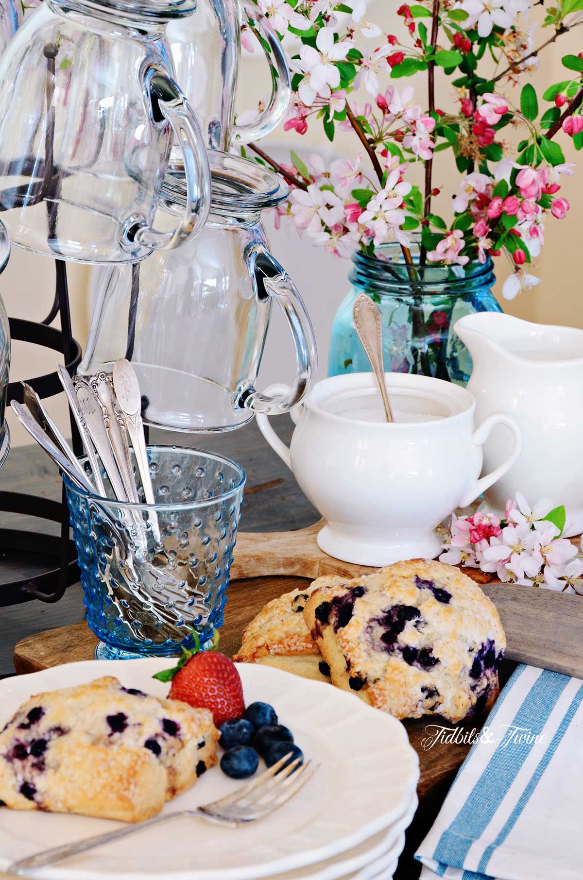 Breakfast vignette showing blueberry scones next to bottle drying rack holding clear glass mugs and pink flowers in the background