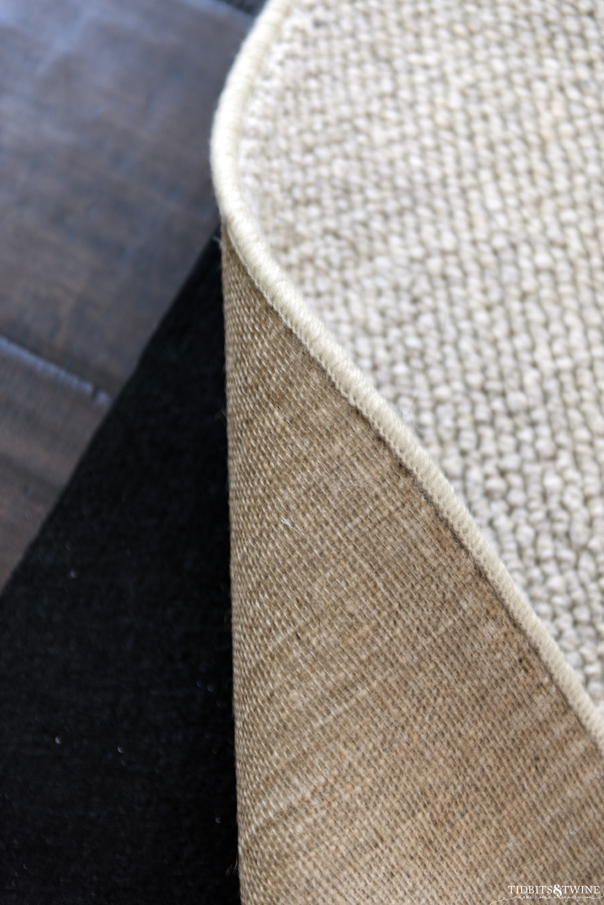 Closeup of underside of wool loop custom rup showing black rug pad underneath on dark wood floor