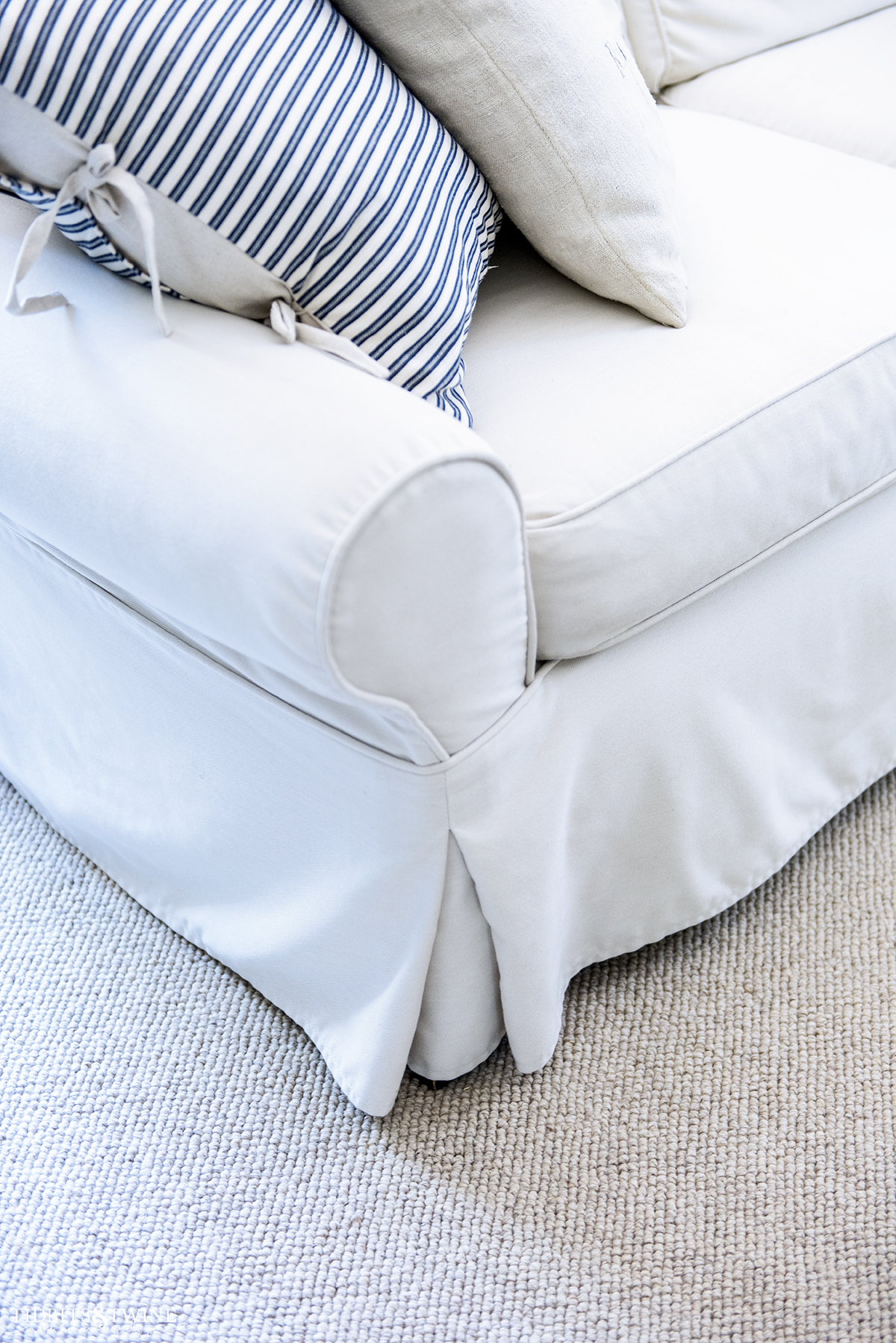 Closeup of white slipcovered sofa on custom wool loop area rug and blue and white stripe pillow