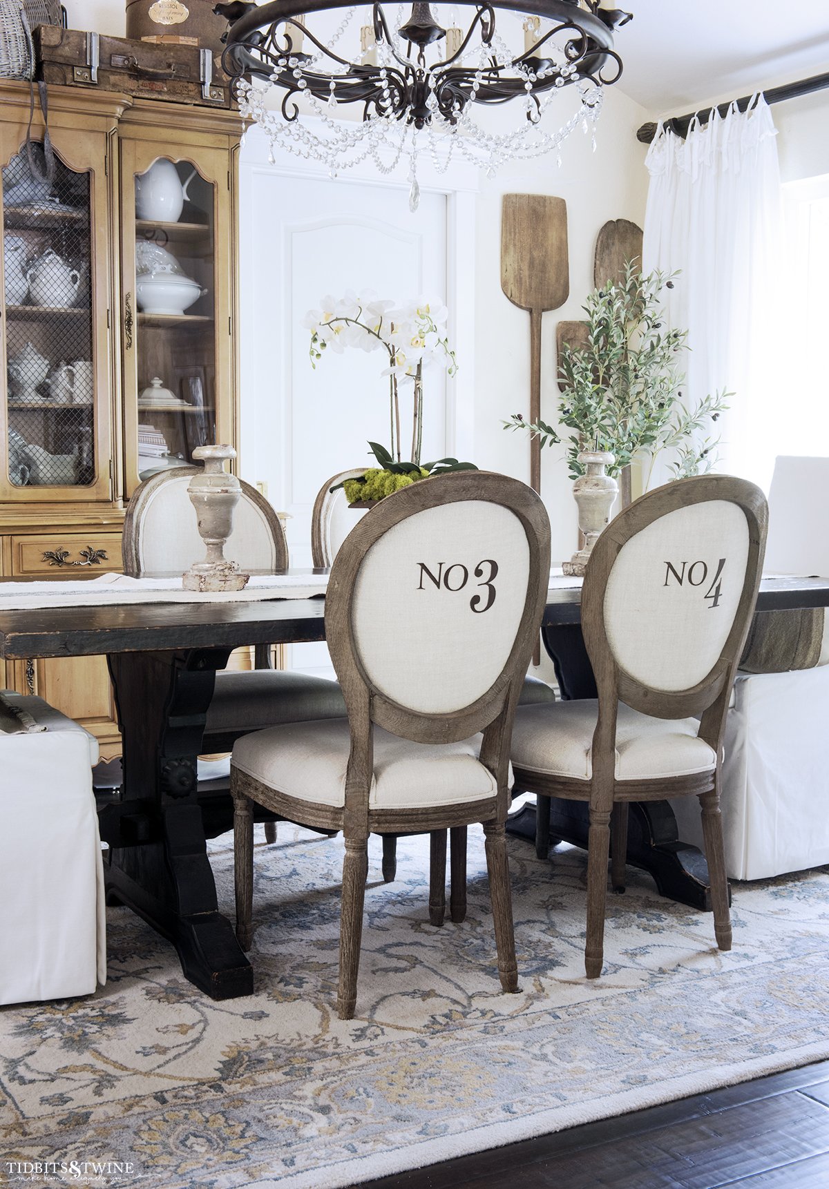 french style dining room with linen and wood chairs with numbers on the back and french hutch containing antique ironstone collection