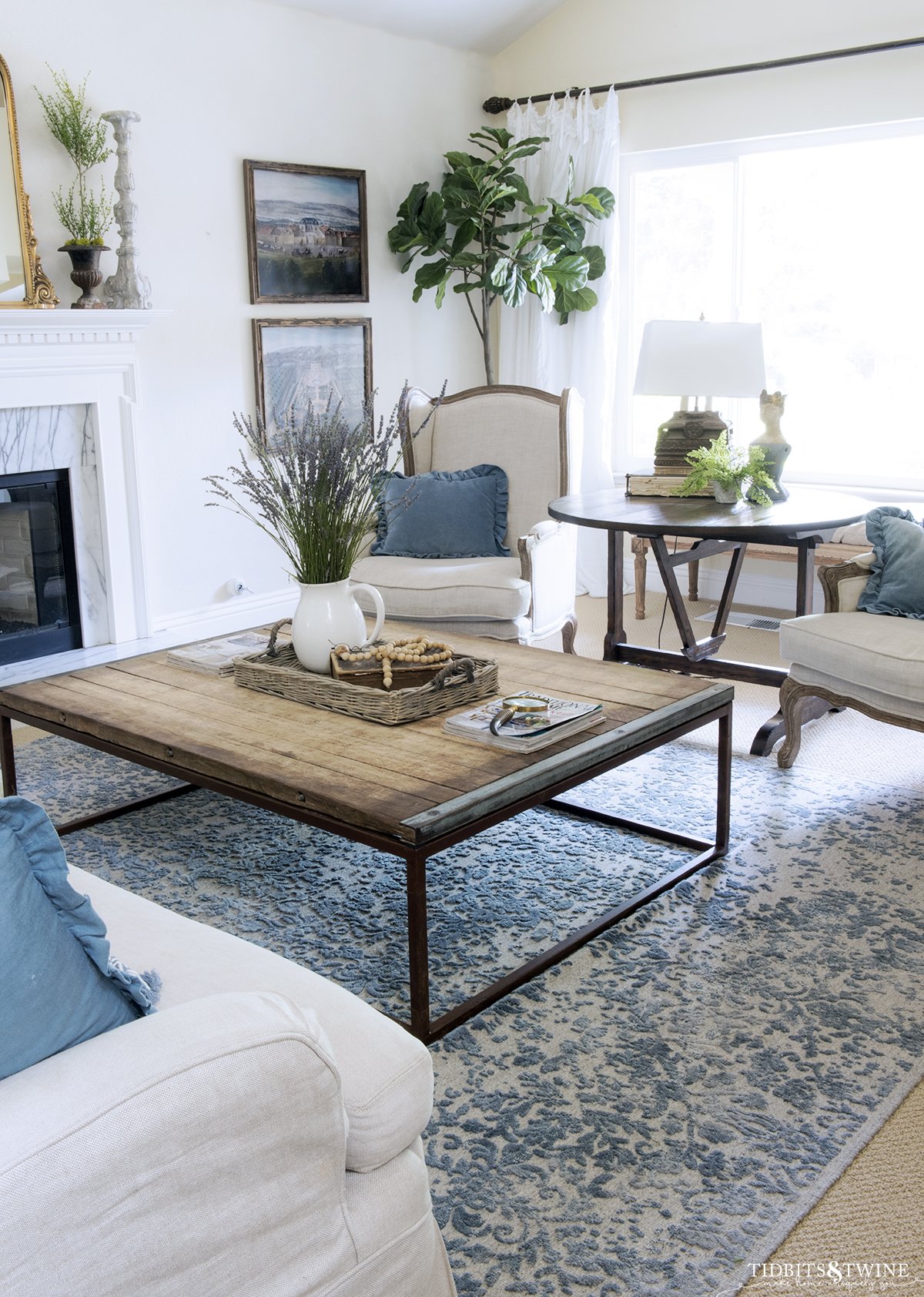 French inspired living room with two wingback chairs and industrial coffee table in front of white marble fireplace