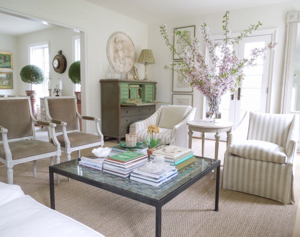 living room with striped slipcovered chairs next to glass square coffee table and gustavian secretary in the background