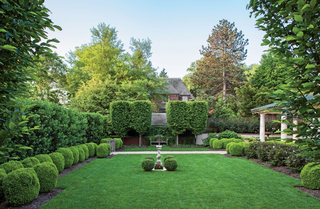 formal backyard garden with lawn surrounded by topiary hedges and antique sundial in center of lawn