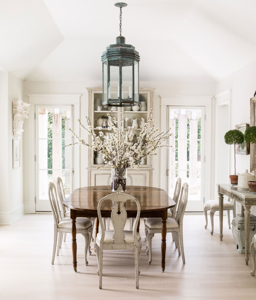 neutral dining room with vaulted ceiling and lantern chandelier over formal table with white gustavian dining chairs