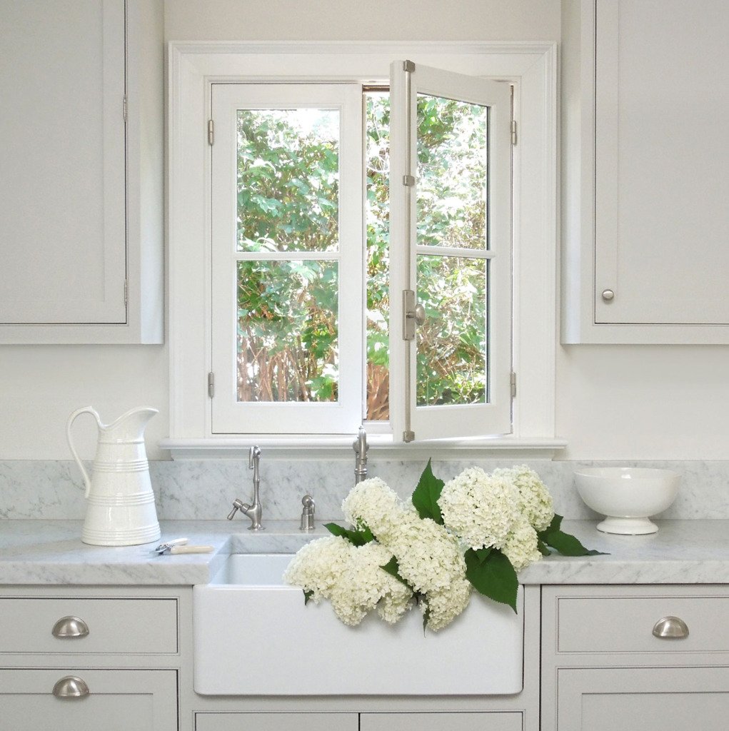 gray inset kitchen cabinets with carrera marble countertop and white farmhouse sink filled with white hydrangeas