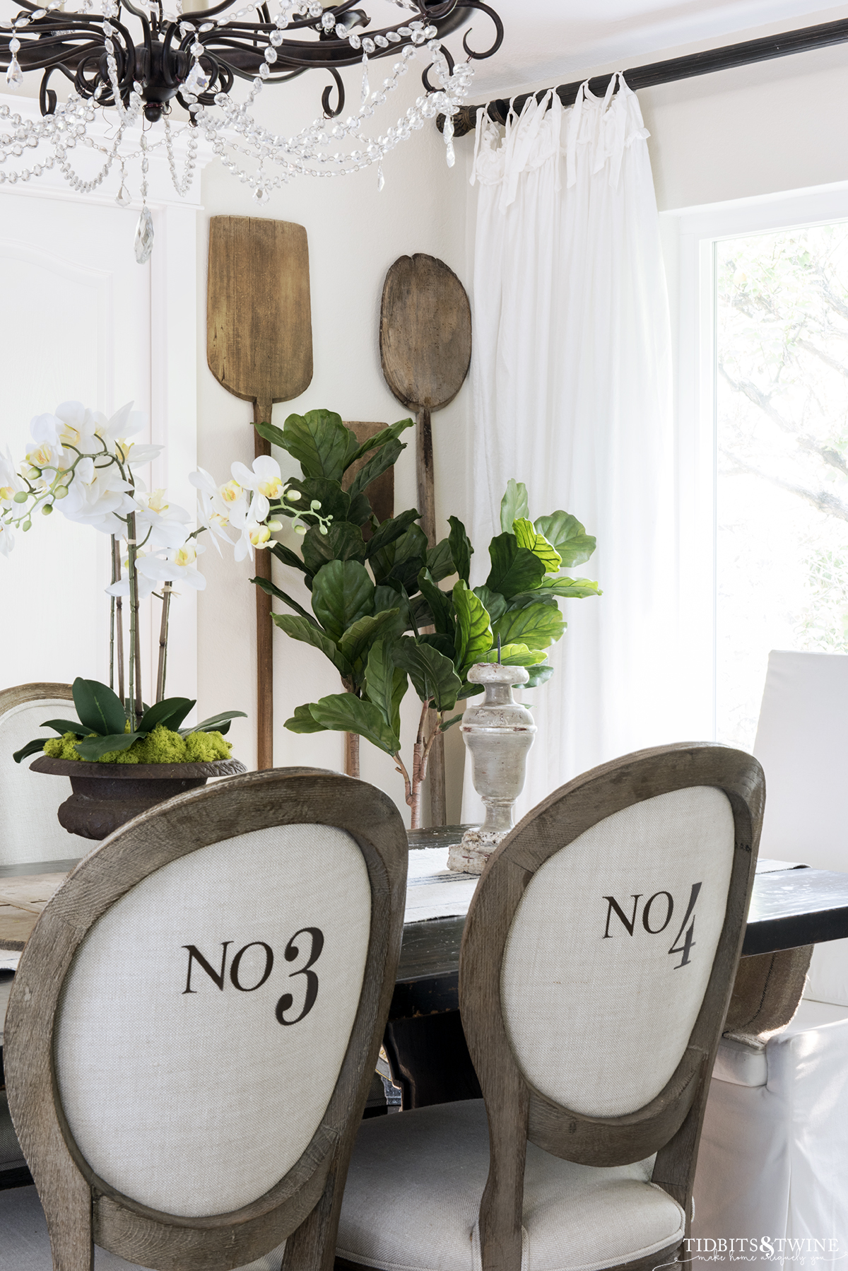 round french linen chairs with numbers on the back in dining room with white orchid on the table and vintage bread paddles hanging on the wall