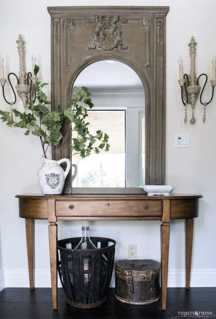 wood demilune console table with green trumeau french style mirror above and french sconces on either side on ballet white painted wall