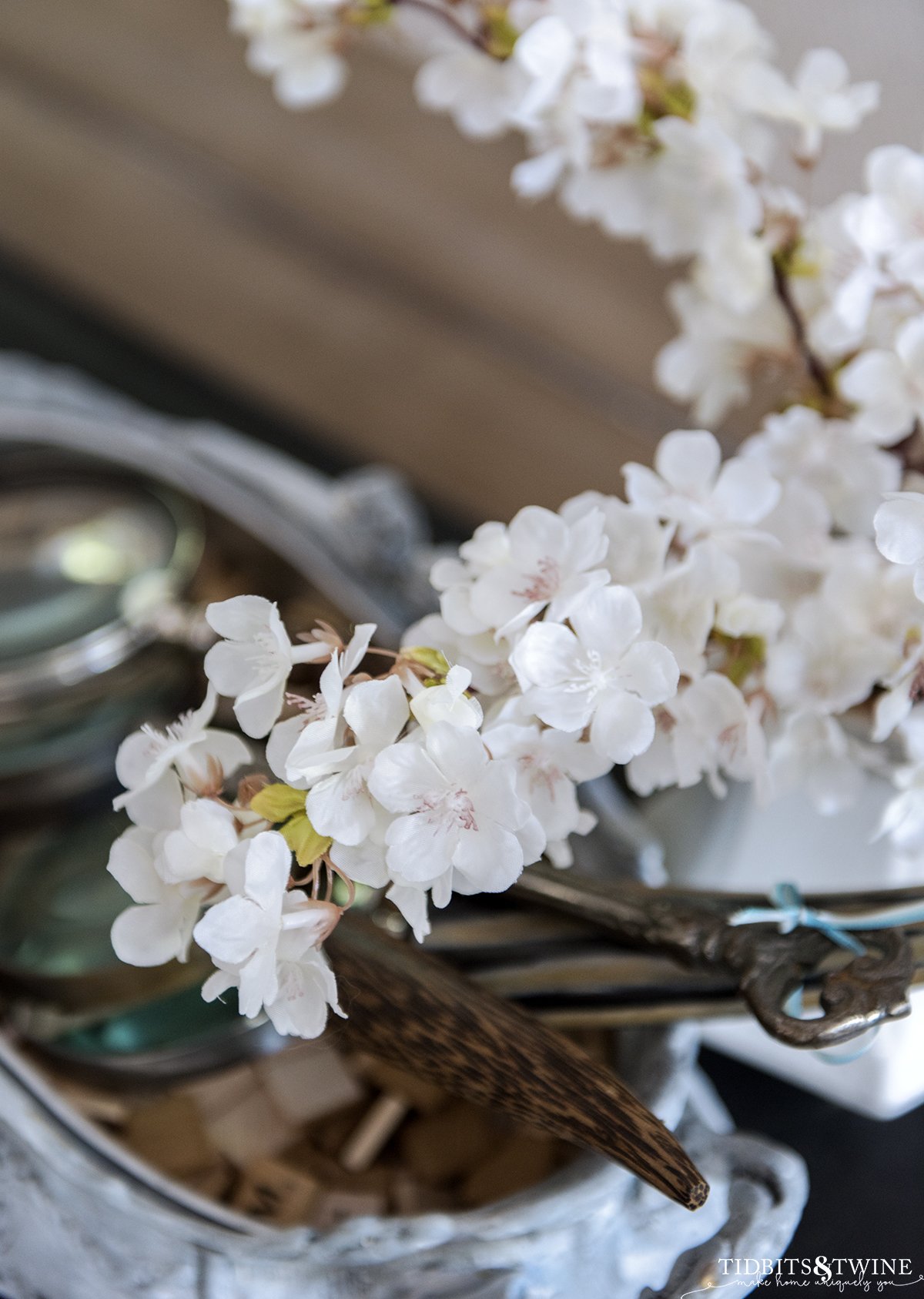 closeup of fake cherry blossom stems that are white with slight pink centers and magnifying glasses in the background