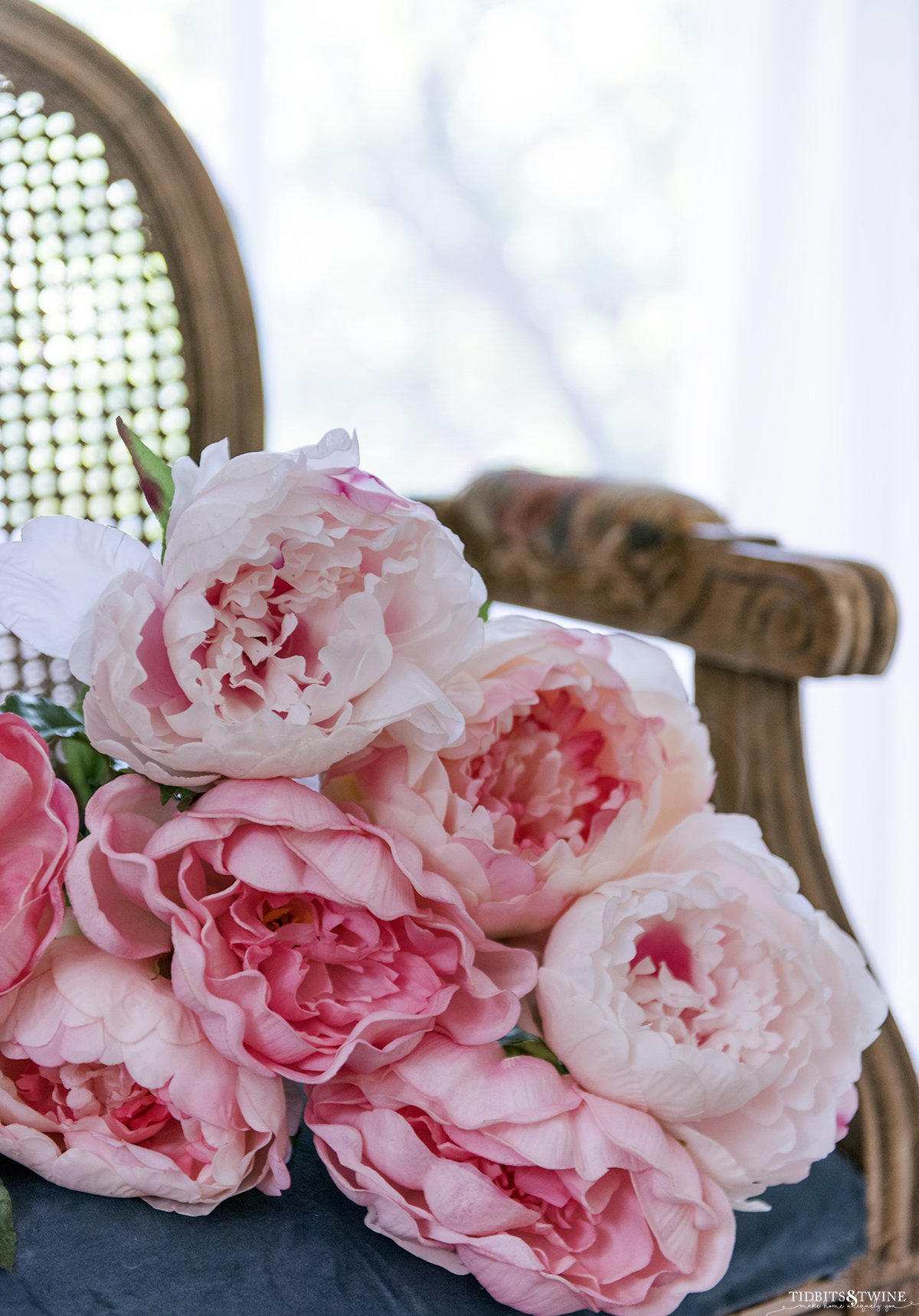 french chair with round cane back and blue velvet seat with a grouping of pink peonies laying on the chair seat