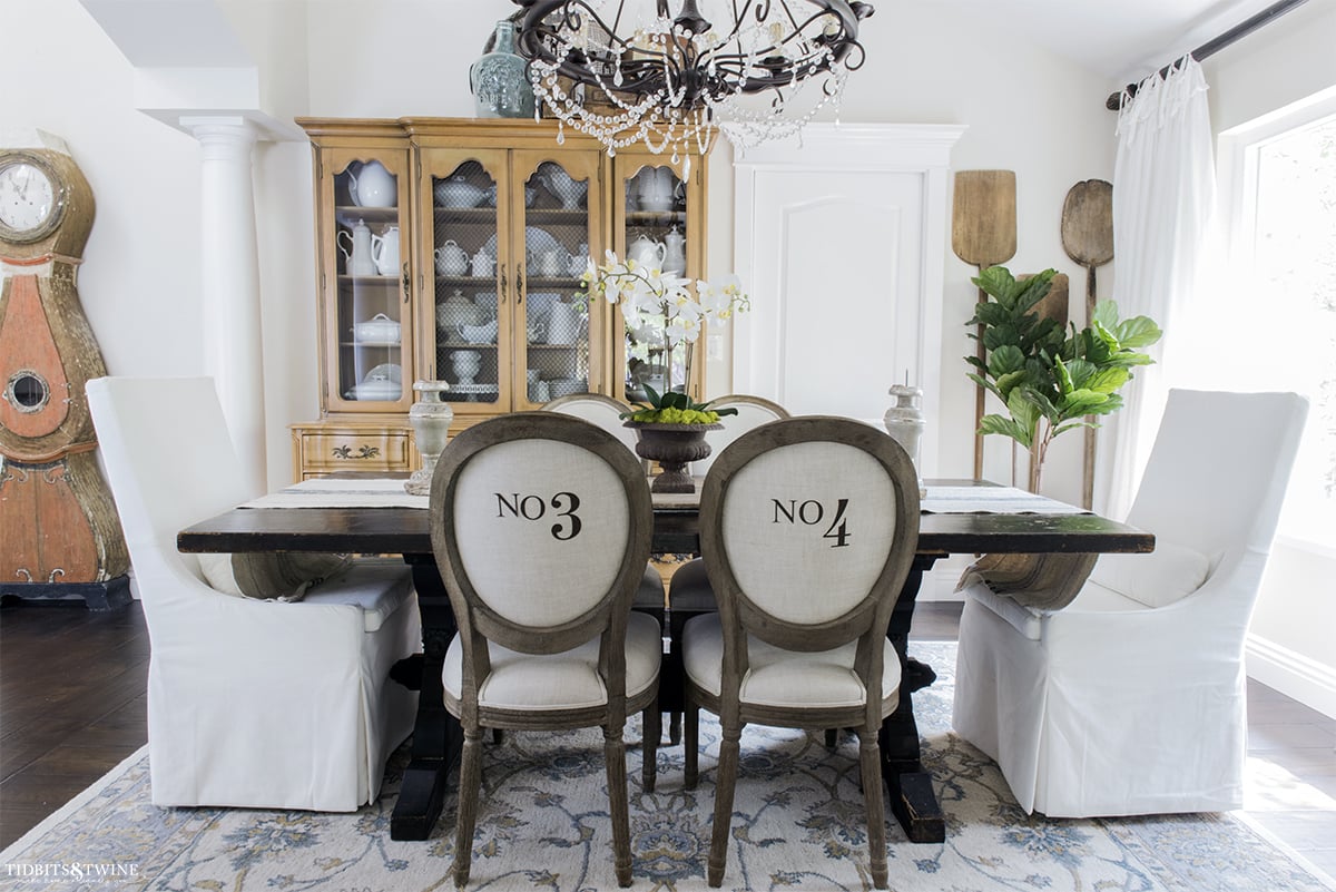 french style dining room with round number chairs white velvet head chairs vintage bread paddles on wall and antique mora clock