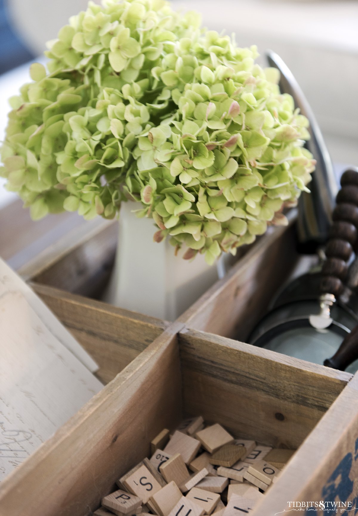 bigleaf hydrangea that has turned green in a vase with magnifying glasses and scrabble tiles as a vignette on coffee table