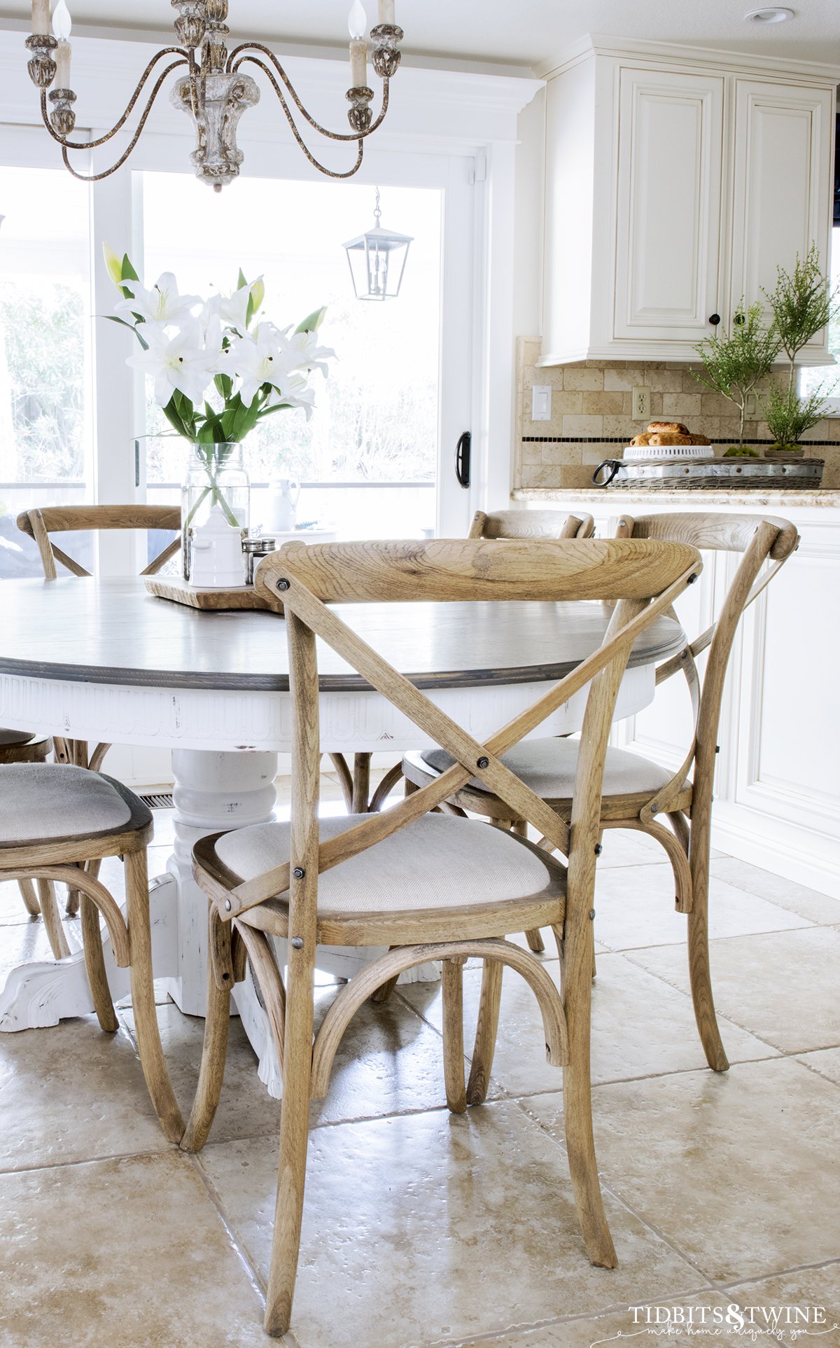 farmhouse kitchen with travertine tile floor and crossback chairs and french country chandelier with white lillies on the table