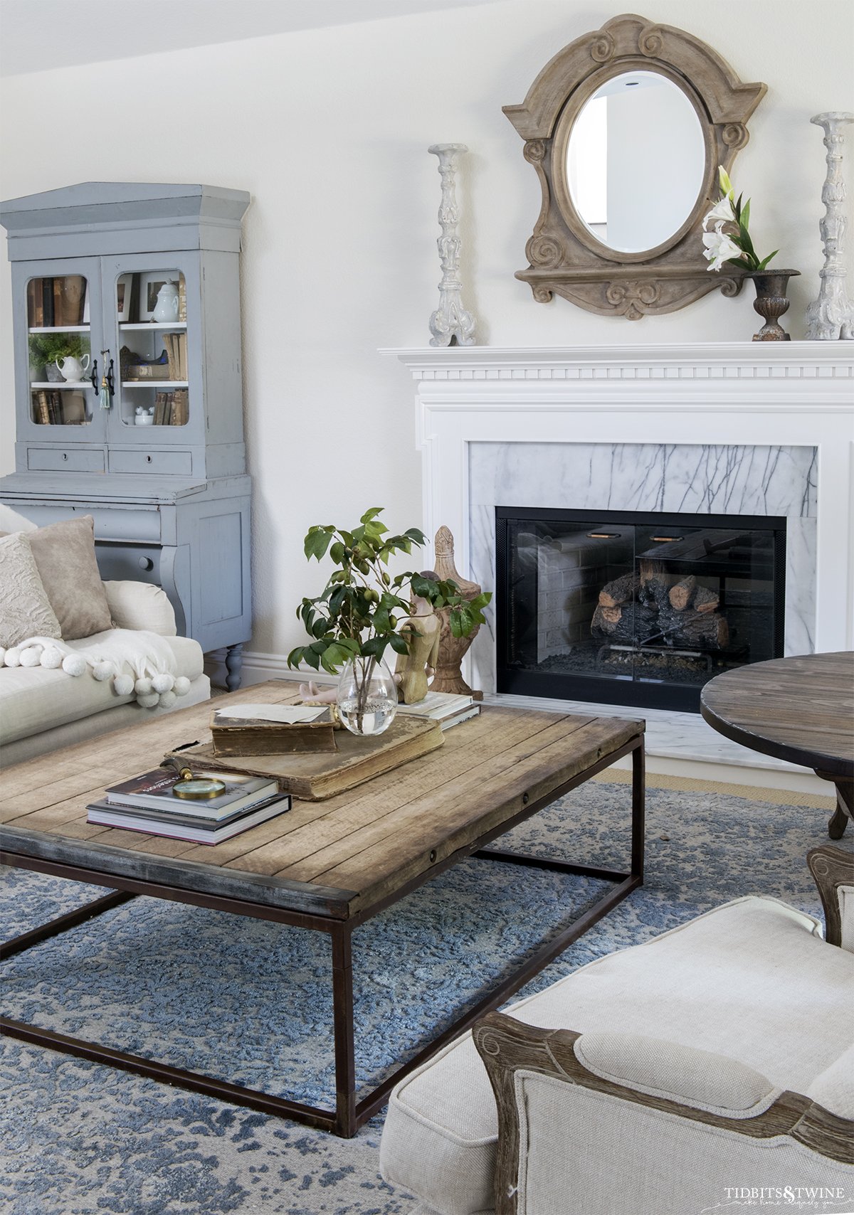 Industrial coffee table in front of white traditional fireplace with french blue cabinet next to it