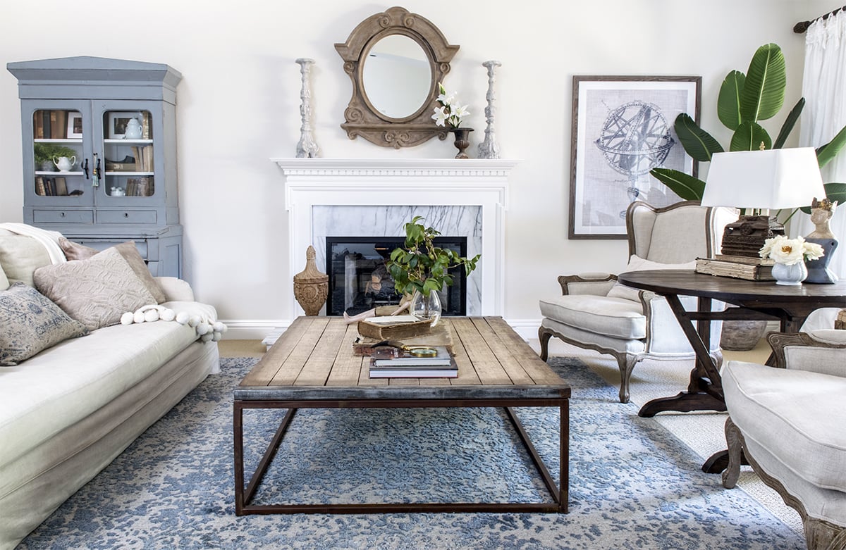 living room with slipcovered linen sofa and french wingback chairs and industrial coffee table on blue rug