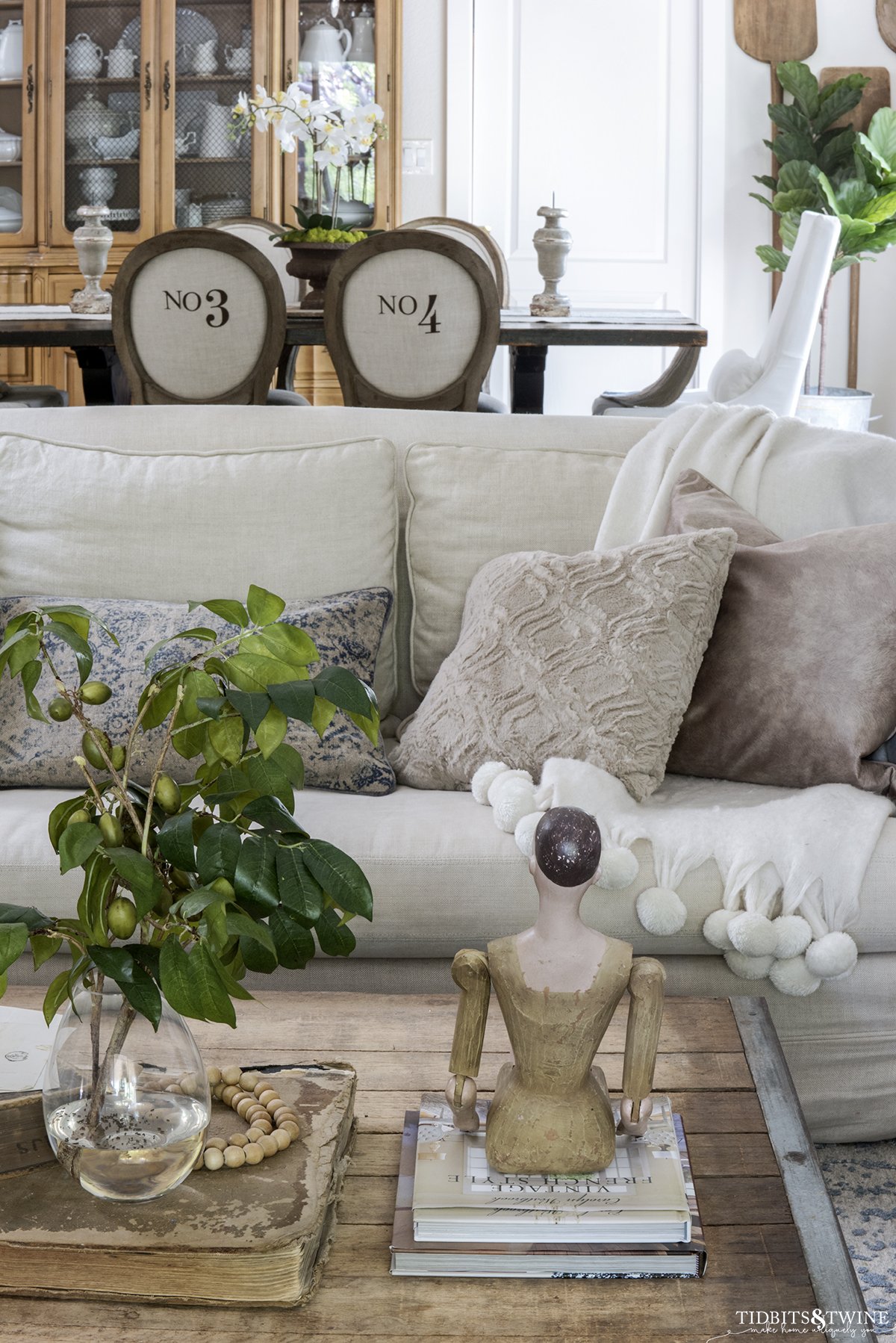 industrial coffee table with santos doll in front of linen sofa with dining room in background with numbered chairs