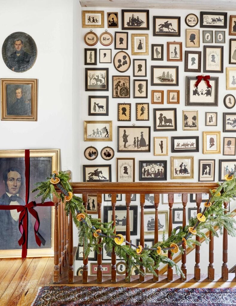 staircase wall filled with silhouette artwork in gold and black frames with christmas  garland on the banister