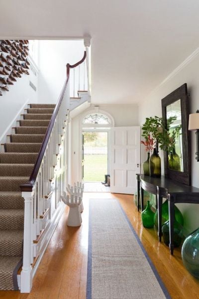 entryway with long hall table with green demijohns underneath and wood floor and stairs with white railing